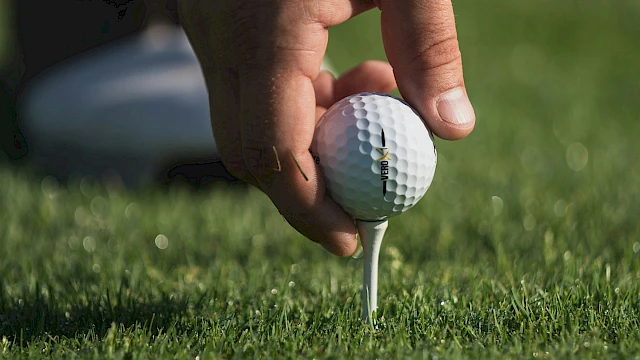 A close-up of a hand placing a golf ball on a tee on a green golf course, preparing for a shot.